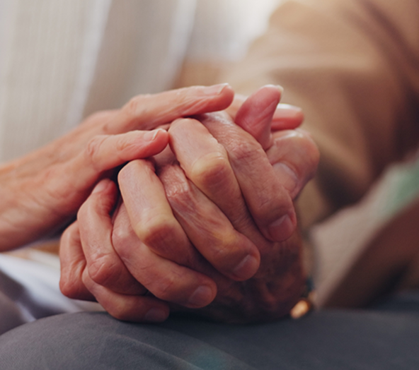 Close-up of two elderly people holding hands, showing gentle support and connection.