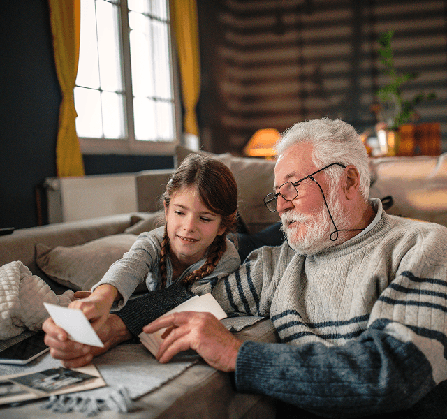 An image of an older man sitting with a young girl looking at photos. They look like they are looking at photos as reminiscing
