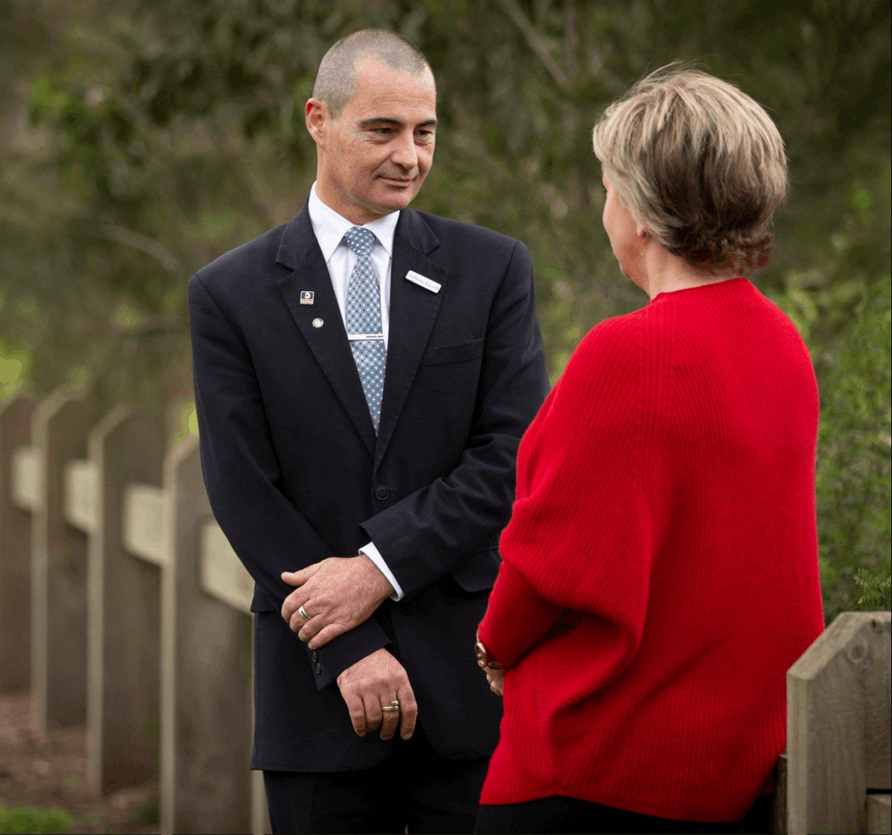 An image of two indviduals with one man in a uniform and a woman with a red sweater. They are facing each other and seems are discussing something